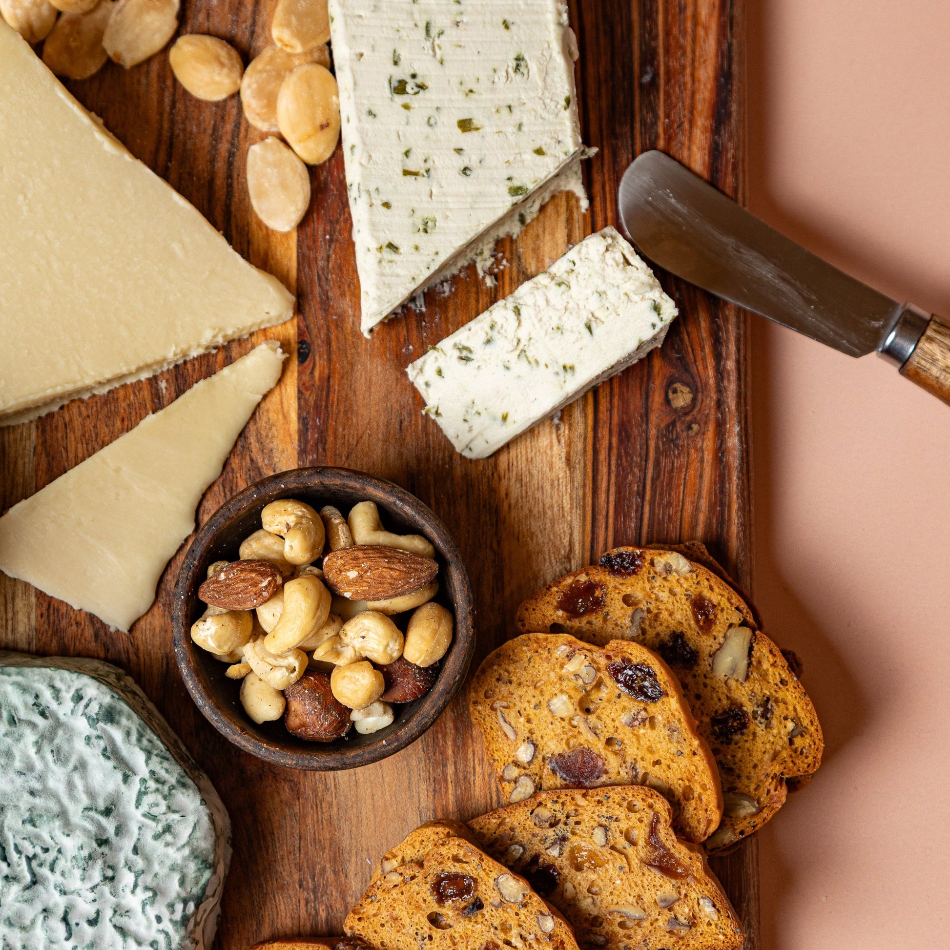 Assorted cheeses, crackers, and nuts on a wooden board with a knife.