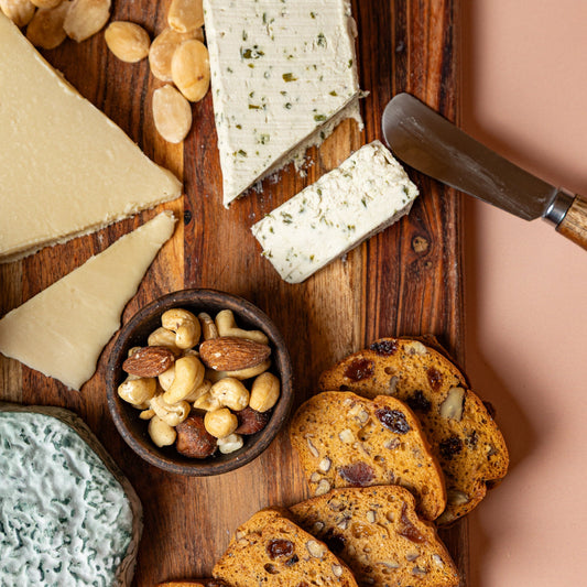 Assorted cheeses, crackers, and nuts on a wooden board with a knife.